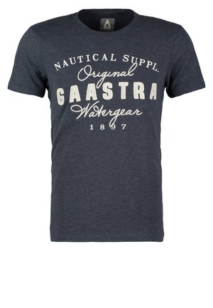 Man loopt en draagt een marineblauw grafisch t-shirt, grijze jeans met omslagen, zwart-grijze sneakers en draagt een grijze jas over zijn schouder.