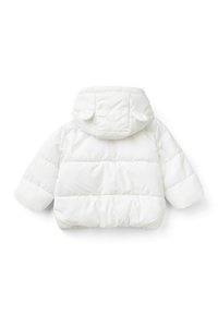 Bílá péřová bunda s kapucí, vyznačující se kulatými akcenty na uších. Prošívaná textura a elastické manžety. Hladký, voděodolný materiál.