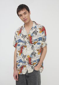 Camicia a manica corta con sfondo crema, decorata con pesci koi colorati, nuvole blu e motivi di palme; tessuto leggero e vestibilità comoda.