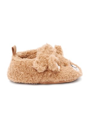 Chausson bébé doux et duveteux de couleur marron clair en forme de chien avec des oreilles et un visage cousu sur le devant, vu de côté.