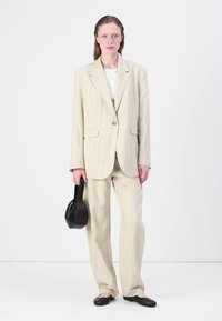 Beige gestreept pak met een blazer met één knoop en rechte broekspijpen, gecombineerd met een zwarte handtas en platte zwarte schoenen.
