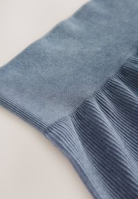 Blå ribbad tyg med en strukturerad yta, som visar en gradvis färgövergång från ljusare till mörkare nyanser och en detalj med rynkad kant.