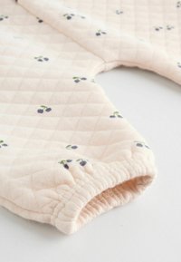 Tessuto trapuntato rosa chiaro con piccoli motivi floreali blu e verdi. Presenta polsini arricciati e una superficie morbida e testurizzata.