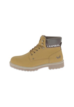 Bota de tobillo de cuero marrón claro con puntera redonda, cuello acolchado gris, ojales de metal y suela de goma texturizada. Presenta el logo en la parte posterior.