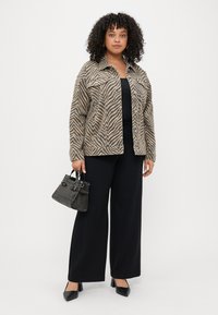 Beige og brun jakke med zebra mønster, sort top, brede sorte bukser og sorte højhælede sko. Lille sort tekstureret håndtaske holdt i hånden.