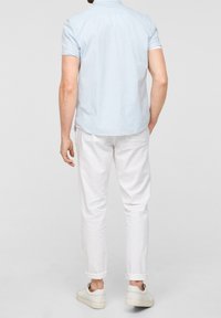 Světlomodrá kostkovaná košile s krátkými rukávy a límcem na knoflíky, doplněná bílými vyhrnutými kalhotami a bílými teniskami.