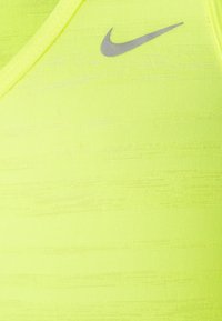 Żółty sportowy biustonosz Nike z dekoltem w serek, wykonany z teksturowanej tkaniny, z małym szarym logo po lewej górnej stronie.