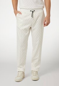 Light-colored jogger pants with a subtle all-over pattern, elastic waistband, side pockets, and black drawstring detail, made of soft fabric.
