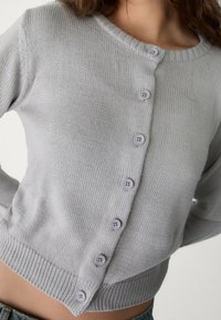 Light grey button-up cardigan made of knitted fabric, featuring ribbed collar and cuffs, six round buttons, and a cropped design.