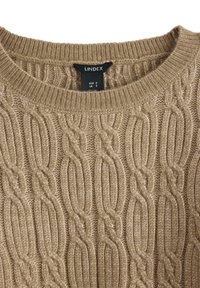 Maglione lavorato a maglia beige con motivo a trecce. Collo rotondo e polsini a coste. L'etichetta mostra le taglie in EUR, UK e US.