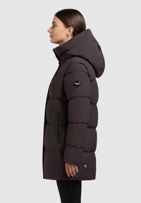 Donker paarse pufferjas met een capuchon, voorzien van zijzakken met rits, geribbelde manchetten en een logo patch op de arm. Gladde textuur en middellange stijl.