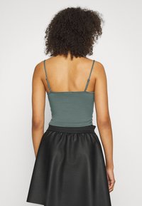 Top teal sem mangas com alças ajustáveis, combinado com uma saia preta de imitação de couro de cintura alta. Textura suave, design ajustado.