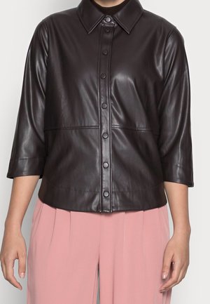 Chemise noire en similicuir à boutons avec manches trois-quarts portée avec un pantalon plissé rose taille haute.