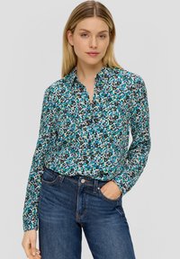 Camicetta button-up con un motivo floreale in tonalità turchese, nera e bianca. Presenta un colletto e maniche lunghe. Abbinata a jeans scuri.