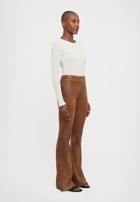 White long-sleeve top paired with high-waisted, flared brown leather pants featuring a circular buckle at the waist. Smooth texture.