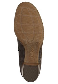 Brązowa zamszowa podeszwa buta z teksturowanym gumowym wzorem i wytłoczonym logo marki. Posiada lekko podniesiony obcas oraz akcenty w postaci przeszyć.