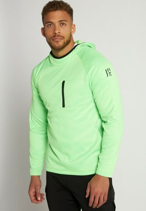 Chemise à manches longues et à capuche de couleur vert menthe vif. Dotée d'une poche poitrine zippée noire et d'un tissu doux et léger avec une texture lisse.