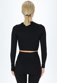 Sort ribbet langærmet cropped top med en tætsiddende pasform. Har en høj halsudskæring og tætsiddende ærmer, parret med højtkalvede leggings.
