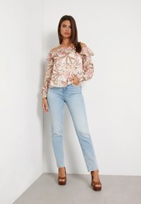 Cvjetna bluzica bez ramena u svijetloružičastoj boji s volanima, u paru sa svijetloplavim ravnim trapericama i smešnim platformama.