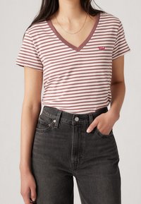 Striped v-neck t-shirt in light pink and white, with a red Levi's logo patch, paired with high-waisted black denim jeans.