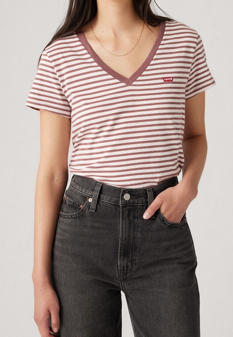 Striped v-neck t-shirt in light pink and white, with a red Levi's logo patch, paired with high-waisted black denim jeans.