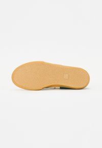 Riepā gumijas pamatne ar teksturētu rakstu, brūngana krāsa, noapaļota forma; satur zīmolu uz sāniem, paredzēta saķeres un izturības nodrošināšanai.