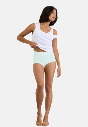 Lichtblauwe hoog getailleerde slip en een wit mouwloos topje van zachte stof. Blootvoets, staand in een ontspannen houding. Eenvoudig ontwerp.