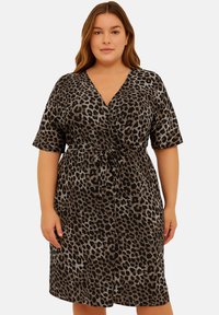 Leopardmönstrad omslagklänning i svart och beige, korta ärmar, V-ringning, självknuten midjedetalj, knälång längd, slät tyggtextur.
