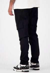 Zwarte cargo-broek met zijzakken, tapered fit en een gladde stofstructuur. Gekocht met gemusterde sneakers met een logodesign.