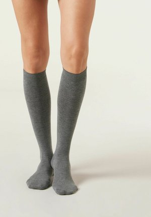 Chaussettes jusqu'au genou en gris foncé, fabriquées dans un matériau doux et lisse, avec une bordure côtelée en haut, dotées d'un design sans couture au niveau des orteils.