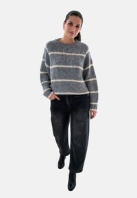 Grijs en wit gestreepte trui van dikke breimaterialen, gecombineerd met donkere, loszittende broek en zwarte enkellaarsjes.