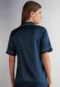 Marinfärgad satinskjorta med korta ärmar, vit piping längs kragen och ärmsluten, slät textur och en avslappnad passform.