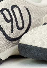 Zapatillas de textura gris claro con un patrón de piel de serpiente, que cuentan con un atrevido bordado negro "90" y una suela de goma negra.