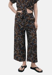Brown wide-leg pants with a leaf pattern in blue and cream, featuring an elastic waistband and soft, lightweight fabric. Paired with black flip-flops.