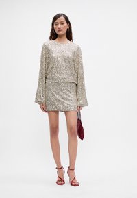 Zlatna dvodelna kombinacija s svilenimi sequini, ki vključuje dolg rokav in mini krilo. Model se je opremil z rdečo biserno torbico in sandali s trakovi.