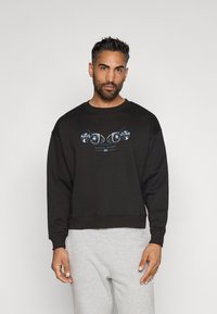 Sweatshirt preto de gola redonda feito de uma mistura de algodão, com um design gráfico de dados na parte frontal. Acentuado com punhos e bainha canelados.