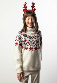 Biały sweter z dzianiny z czerwonymi i granatowymi geometrycznymi oraz kwiatowymi wzorami; wysoki kołnierz; w połączeniu z beżowymi spodenkami z prążkowanej tkaniny; nosi czerwone poroże renifera.