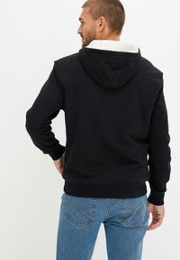 Hoodie nero con cappuccio foderato in bianco, dotato di maniche lunghe e vestibilità comoda. Indossato con jeans in denim blu.