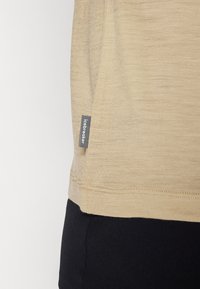 Camisa de manga corta de color marrón, hecha de un tejido fino y texturizado, con una etiqueta negra visible en la costura lateral. El dobladillo es recto y tiene costuras cuidadas.