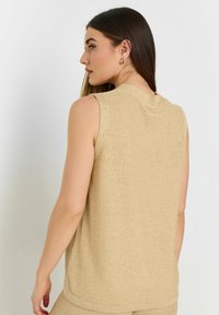 Ljus beige ärmlös stickad topp med texturerad yta, hög halsringning och lös passform, med en enkel design på baksidan.