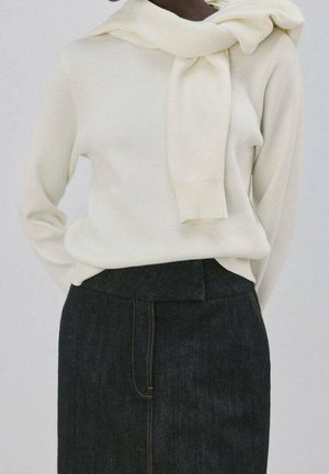 Persoon draagt een witte trui met nog een witte trui over de schouders gedrapeerd, gecombineerd met een high waist donker denim rokje.