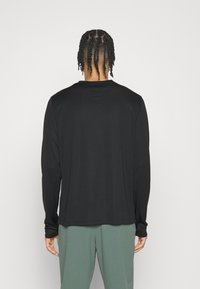 Svart långärmad tröja med rund halsringning, slät textur och avslappnad passform, ihopparad med gröna byxor. Inga synliga märken eller tryck.