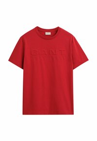 T-shirt di cotone rosso con scollo rotondo e maniche corte. La parte anteriore presenta un logo in rilievo. Texture liscia, design casual.