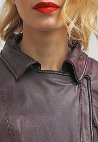 Burgundy läderjacka med krage, med en slät textur och skräddarsydd design. Sömnadsdetaljer synliga nära nackområdet.