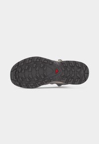 Μαύρη σόλα παπουτσιού από καουτσούκ με βαθιά αυλάκια και κόκκινο τριγωνικό λογότυπο στο κέντρο, σχεδιασμένη για πρόσφυση και ανθεκτικότητα.