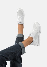 Sneakers bianchi con tomaia strutturata, con accenti in rete grigia e lacci, abbinati a jeans di denim arrotolati con orli sfrangiati.