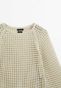 Beige Baumwollpullover mit offenem Strickdesign, rundem Halsausschnitt und langen Ärmeln, der eine lockere, atmungsaktive Textur zeigt.