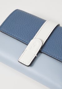 Portafoglio in pelle blu e azzurro con una superficie superiore testurizzata, chiusura e fascia bianchi, e una sezione inferiore liscia.