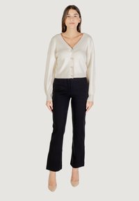 Cardigan de canalé crema con botones frontales, combinado con pantalones negros ajustados. La modelo lleva tacones nude. Diseño simple y moderno.