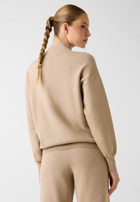 Beige gebreide trui met een hoge hals, doorgezakte schouders en geribbelde manchetten, gecombineerd met bijpassende broek voor een samenhangende look.